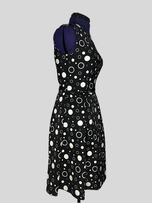 Asymmetric dress with white polka dot patterns on a black background, and pleated skirt, displayed on a mannequin.