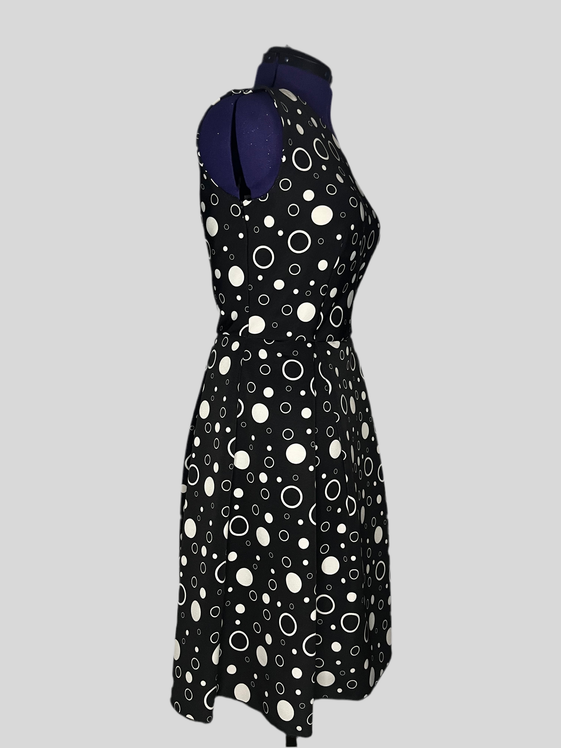 Asymmetric dress with white polka dot patterns on a black background, and pleated skirt, displayed on a mannequin.