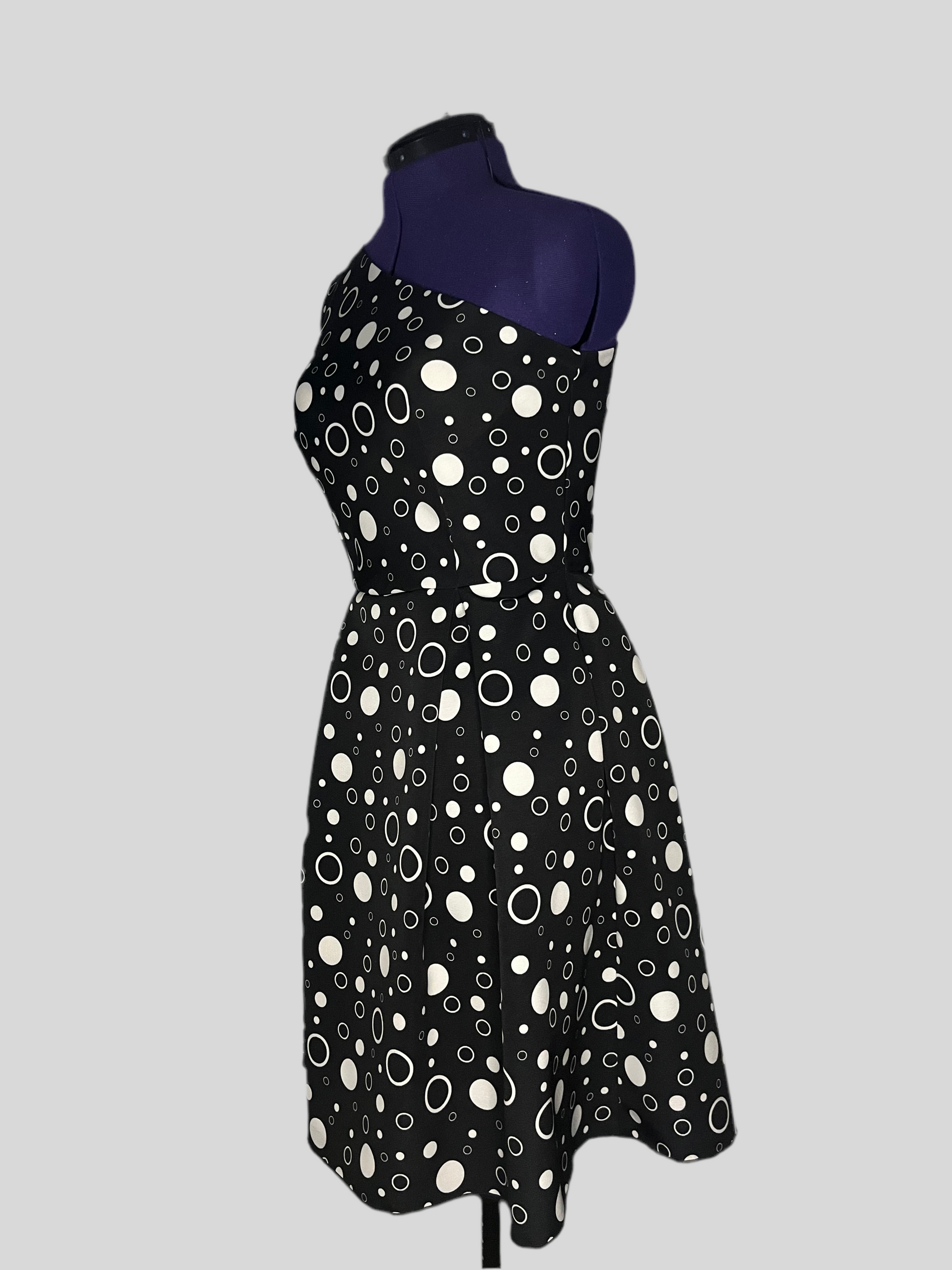 Asymmetric dress with white polka dot patterns on a black background, and pleated skirt, displayed on a mannequin.