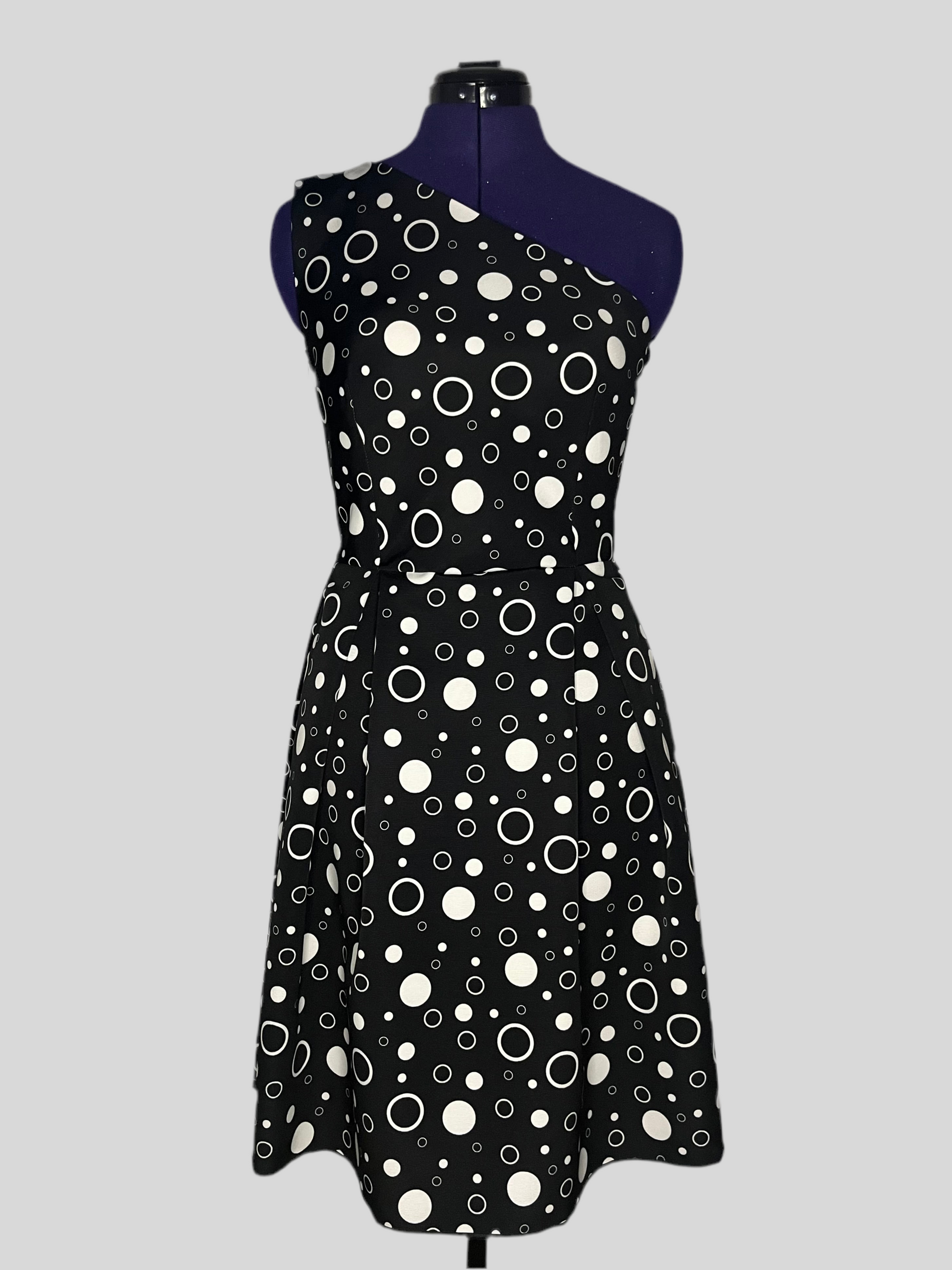Asymmetric dress with white polka dot patterns on a black background, and pleated skirt, displayed on a mannequin.