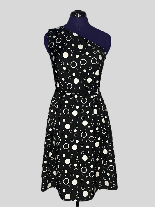 Asymmetric dress with white polka dot patterns on a black background, and pleated skirt, displayed on a mannequin.