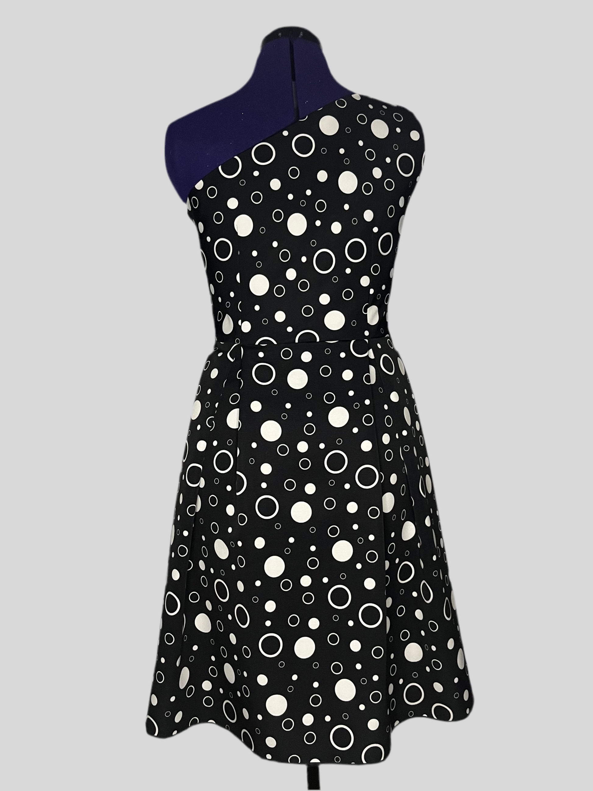 Asymmetric dress with white polka dot patterns on a black background, and pleated skirt, displayed on a mannequin.
